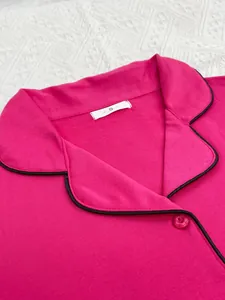 Détail en gros plan du col de pyjama rose pour femme avec passepoil noir et bouton fleur