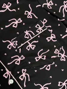Détail d'un pyjama noir avec motif de nœuds roses et passepoil sur la poche