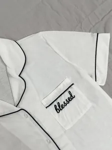 Gros plan du haut de pyjama blanc avec liseré noir et broderie blessed sur la poche
