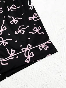 Gros plan sur le tissu de pyjama noir avec de jolis motifs de nœuds et cœurs roses.