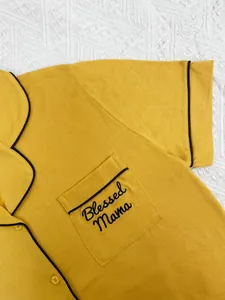 Détail en gros plan de la broderie Blessed Mama sur la poche du pyjama jaune à passepoil