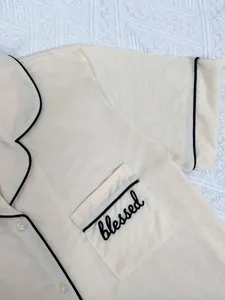 Gros plan du haut de pyjama crème pour femme avec passepoil noir et broderie blessed sur la poche