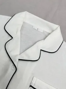 Gros plan détaillé d'un haut de pyjama blanc pour femme avec liseré noir et une poche
