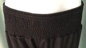 Macro view showing the high elastic smocked waistband of black harem yoga pants.