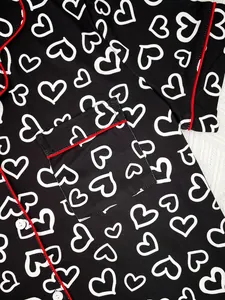 Close-up of black pajama top featuring white heart patterns and red piping detail