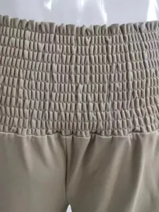 Close-up detail of the high-waisted smocked elastic waistband on beige harem pants
