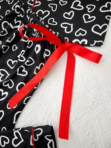 Close-up detail of black heart print pajama pants with a vibrant red satin ribbon bow.