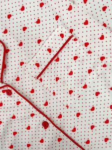 Detailed close-up of red heart polka dot pattern and piping on soft white nightwear fabric