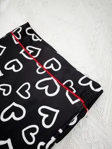 Detail of black heart-print pajama set with elegant red piping and soft fabric texture.