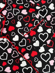 Close-up detail of women's pajamas with vibrant heart print and elegant red piping