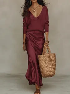 Détail d'un pull en maille bordeaux sur une robe en satin avec un sac en paille.