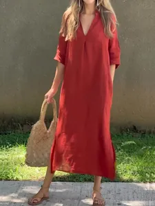 Full view of red linen maxi dress with front pleats and side slits styled with a straw bag.
