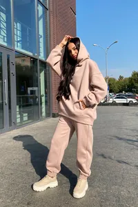 Femme posant en extérieur avec un sweat à capuche beige élégant et un ensemble de jogging.