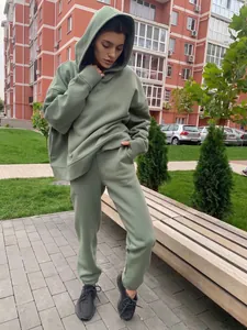 Ensemble sweat à capuche et jogging vert sauge porté par un mannequin en milieu résidentiel.