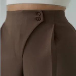 Detailansicht des Taillenbereichs einer braunen High-Waist-Stoffhose mit zwei Knöpfen