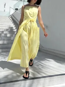 Elegant yellow sleeveless sun dress with waist tie and pockets on outdoor stairs.