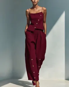 Model wearing a burgundy two-piece outfit with decorative buttons in a sunlit room.