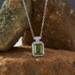 Close-up of rectangular green gemstone pendant with silver halo on rock background