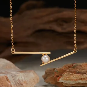 Close-up of geometric gold bar necklace featuring a single natural white pearl