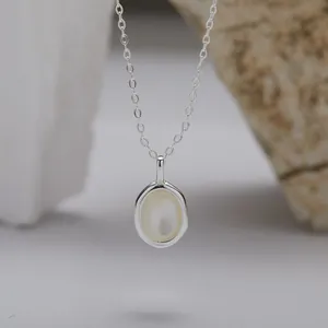 Makro-Detail einer S925 Silberkette mit einem eleganten ovalen weißen Muschel-Anhänger.