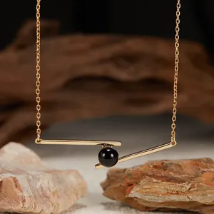 Detailed macro view of a geometric gold bar pendant necklace with a black onyx bead