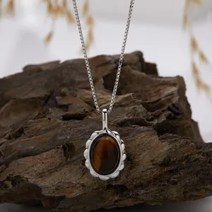 Close-up of a tiger eye gemstone pendant on a silver box chain against a natural wood bark.