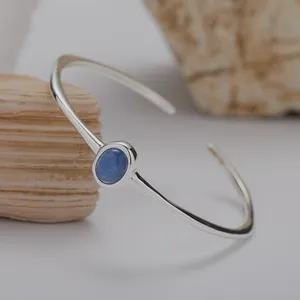 Detailaufnahme eines S925 Silberarmreifs mit einem blauen Edelstein auf Naturstein