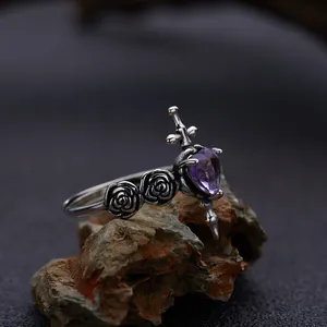Close-up of gothic silver ring with sword piercing a purple heart and rose details