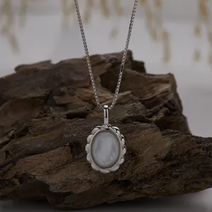 Close-up of elegant S925 sterling silver necklace with oval white shell pendant on rock