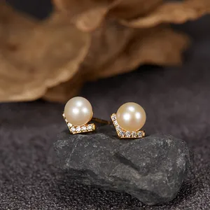 Detail shot of V-shaped gold stud earrings with freshwater pearls and crystals on rock