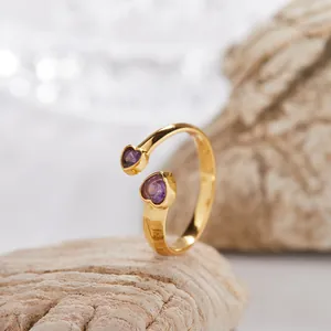 Primo piano di un anello aperto dorato con due gemme viola a forma di cuore in argento 925