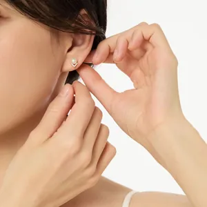 Close-up of elegant V-shaped pearl stud earring worn by a model on white background.