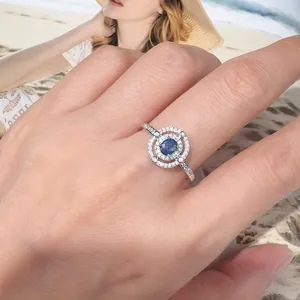 Nahaufnahme eines eleganten S925 Silberrings mit blauem Saphir und glitzerndem Pavé-Halo.