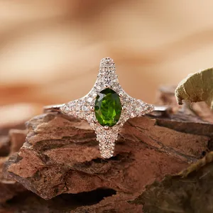 Dettaglio macro di un anello a stella in argento con gemma verde su legno naturale