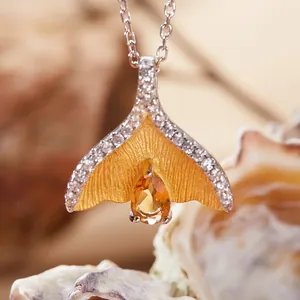 Close-up van een gouden vissenstaart hanger ketting met een peervormige gele steen
