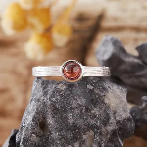 Primo piano di un anello in argento e granato con trama legno su roccia vulcanica