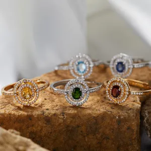 Nahaufnahme eleganter Halo-Ringe mit farbenfrohen Edelsteinen auf strukturiertem Stein