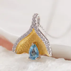 Close-up van een zilveren walvisstaart hanger met een peervormige blauwe edelsteen