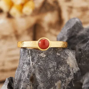 Dettaglio di un anello in argento S925 dorato con gemma rossa e trama a corteccia