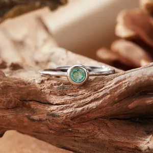 Detail shot of a minimalist S925 silver ring with a brilliant round green gemstone.