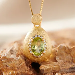 Close-up of a luxury brushed gold teardrop pendant featuring an oval green gemstone.
