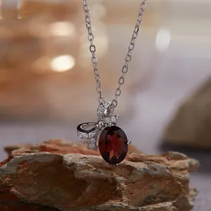 Detailopname van S925 zilveren strik ketting met rode granaat op een rotsblok.