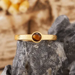 Primo piano di un anello dorato testurizzato con una pietra occhio di tigre tonda.