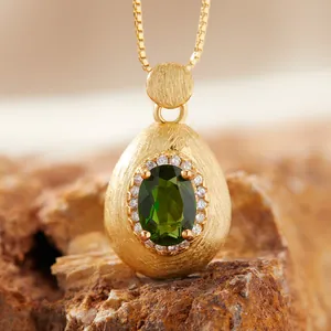 Detailed macro view of brushed gold egg pendant with green gemstone and zircon halo