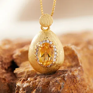 Close-up of elegant citrine gemstone pendant with brushed gold finish on natural rock.