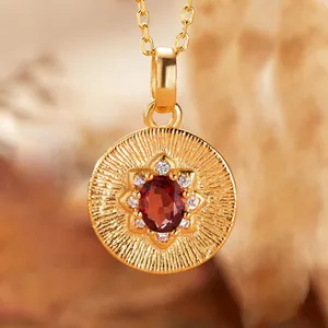 Close-up detail of a gold sunburst pendant featuring an oval red garnet gemstone
