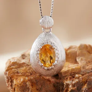 Macro view of teardrop brushed silver pendant featuring a faceted oval citrine gemstone