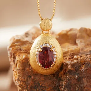 Close-up of teardrop brushed gold pendant with oval red garnet and white zircon accents.