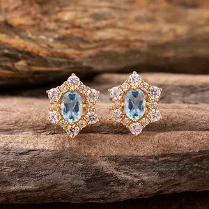Close-up detail of elegant gold flower stud earrings with oval blue gemstone and crystals