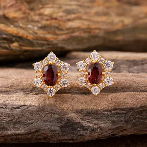 Macro detail of sunflower-shaped gold earrings with red garnet center and clear halo.